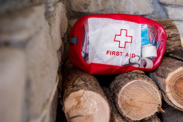 Clear red first aid kit resting on a stone wall and a pile of chopped firewood.