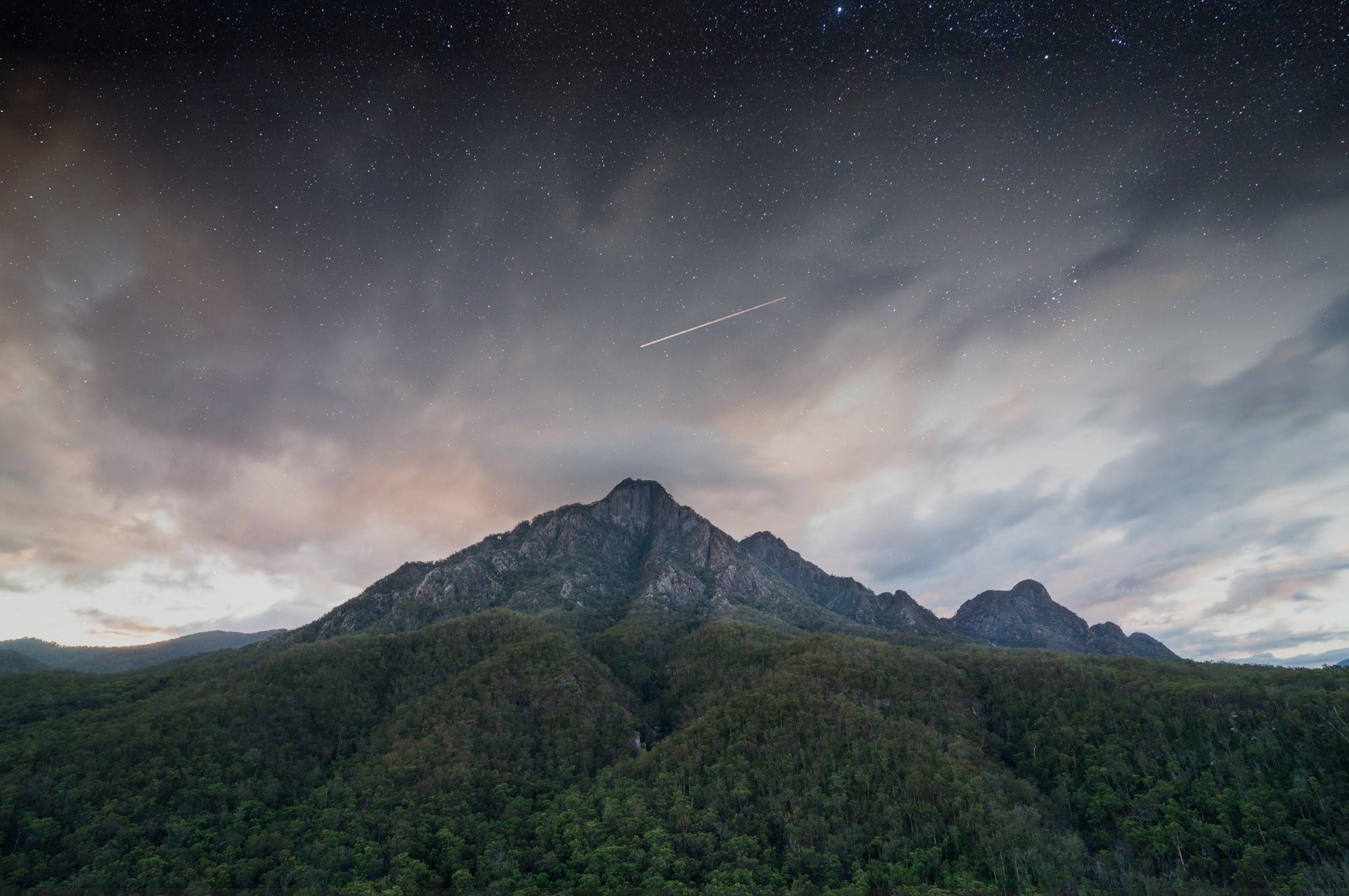 A night photo of Mount Barney located in the Scenic Rim Queensland. A shooting star is seen over the peak of the mountain amongst the starry night sky